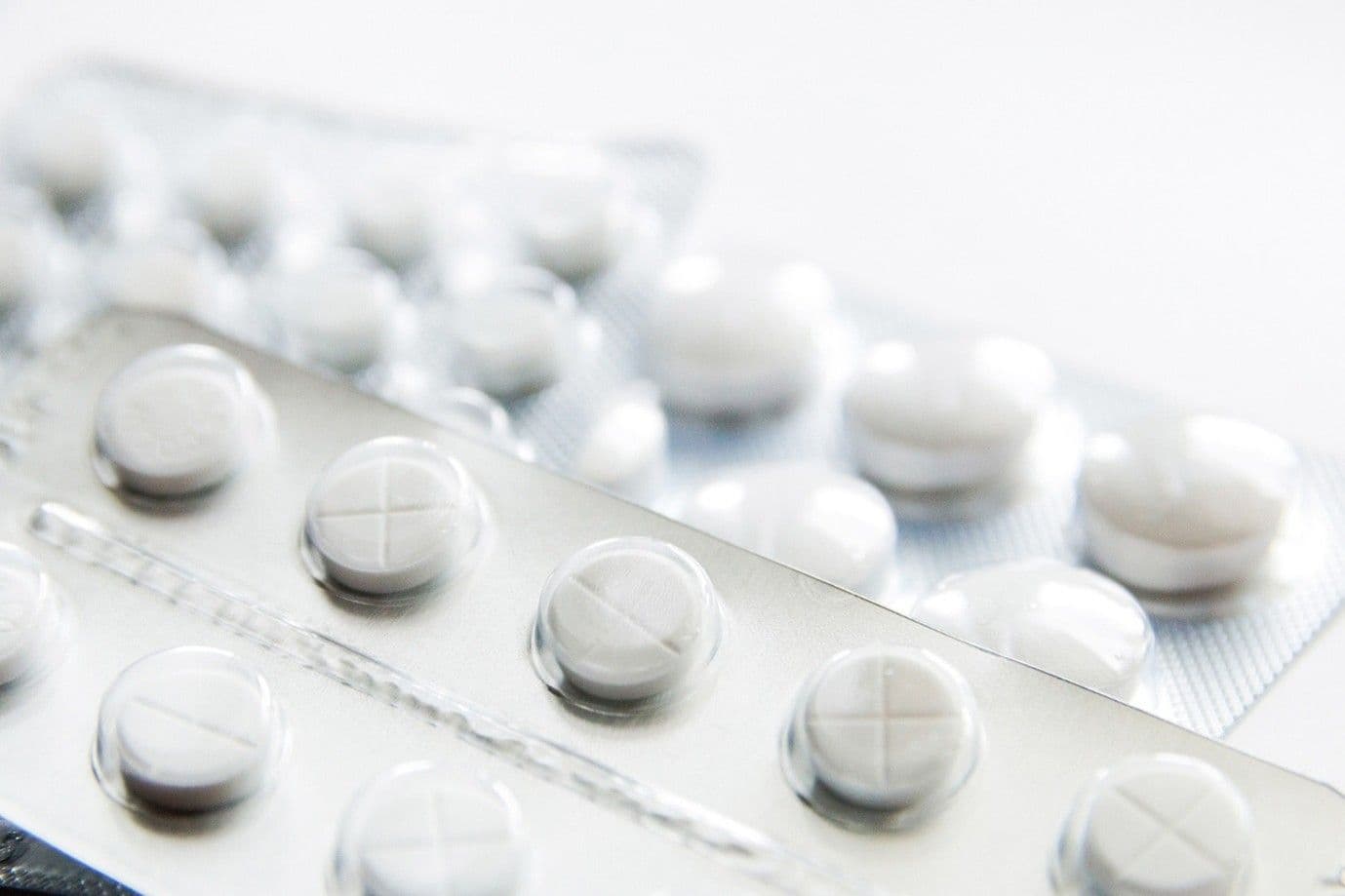 Close-up of blister packs containing round, white tablets with cross imprints, arranged on a light background.