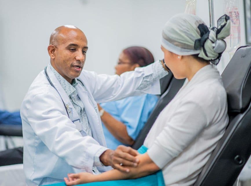 Male clinician attending to a female patient sitting up on hospital bed