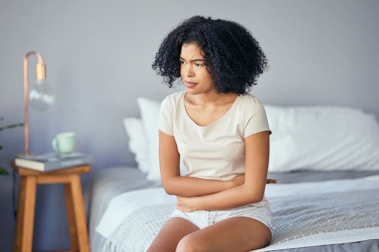 A woman, sat on the edge of her bed, holding her stomach