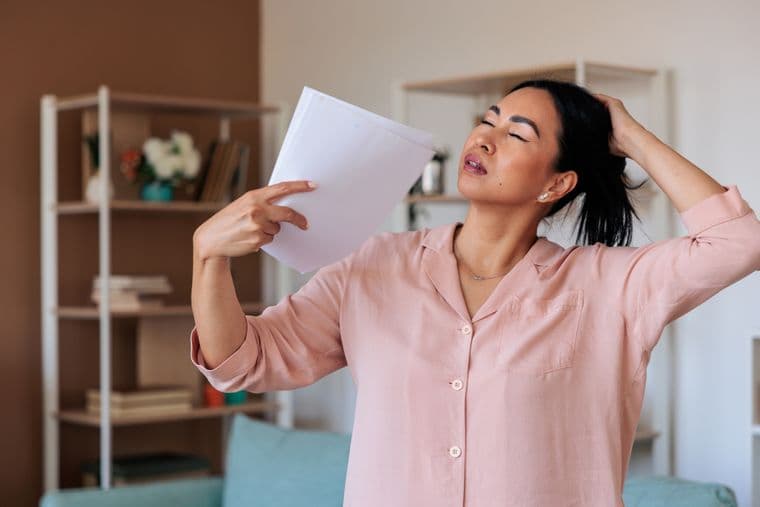 Woman having a hot flush, fanning herself with papers
