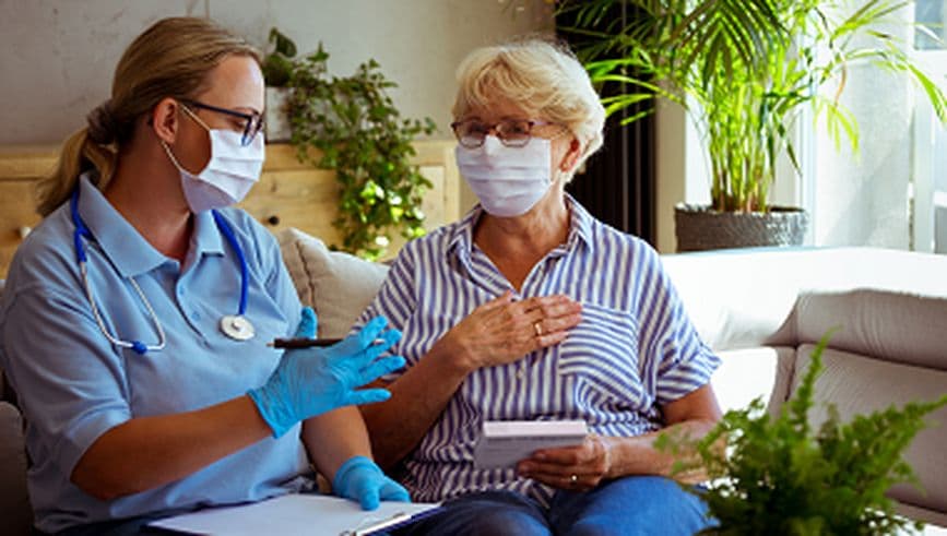 Nurse on home visit with older female patient, with both wearing facemasks