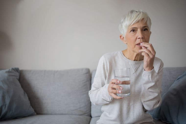 An older woman taking a pill with a glass of water