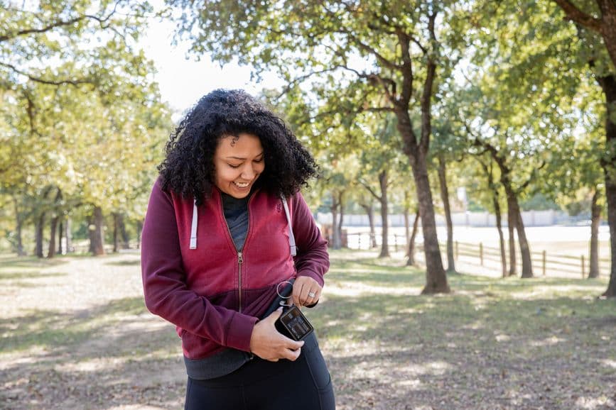A woman, in a park, uses a piece of medical technology