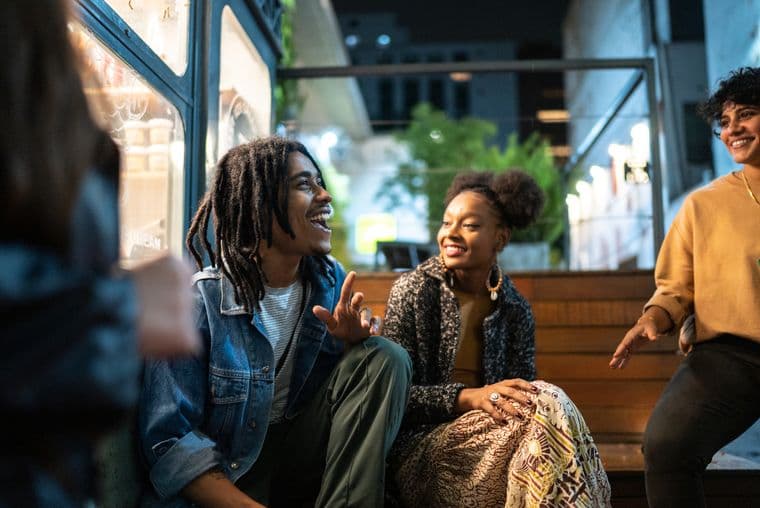 Three young people chatting and laughing in an outside dining area at night